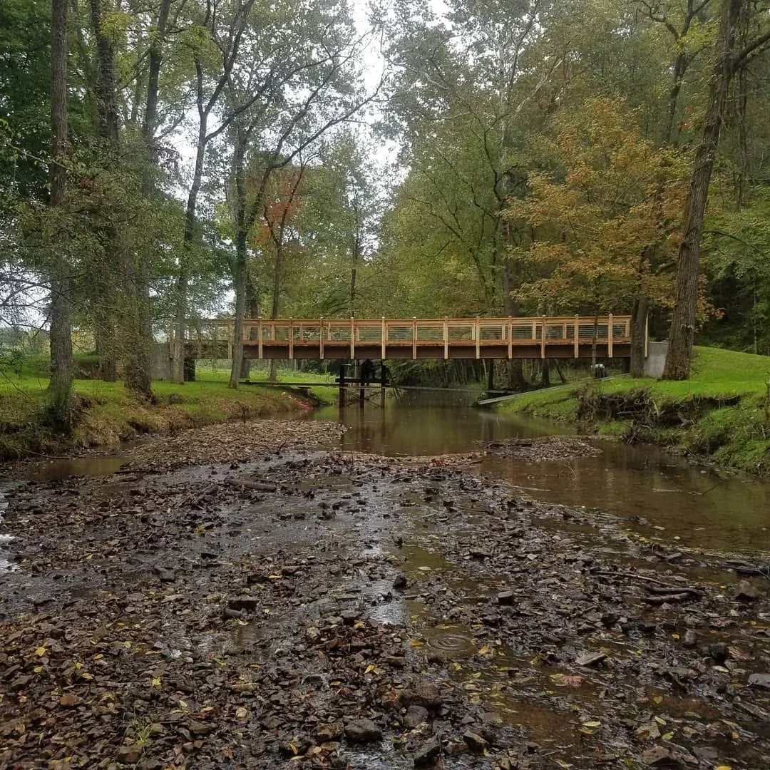 Wooden pedestrian bridge with timber railings spanning creek in wooded setting