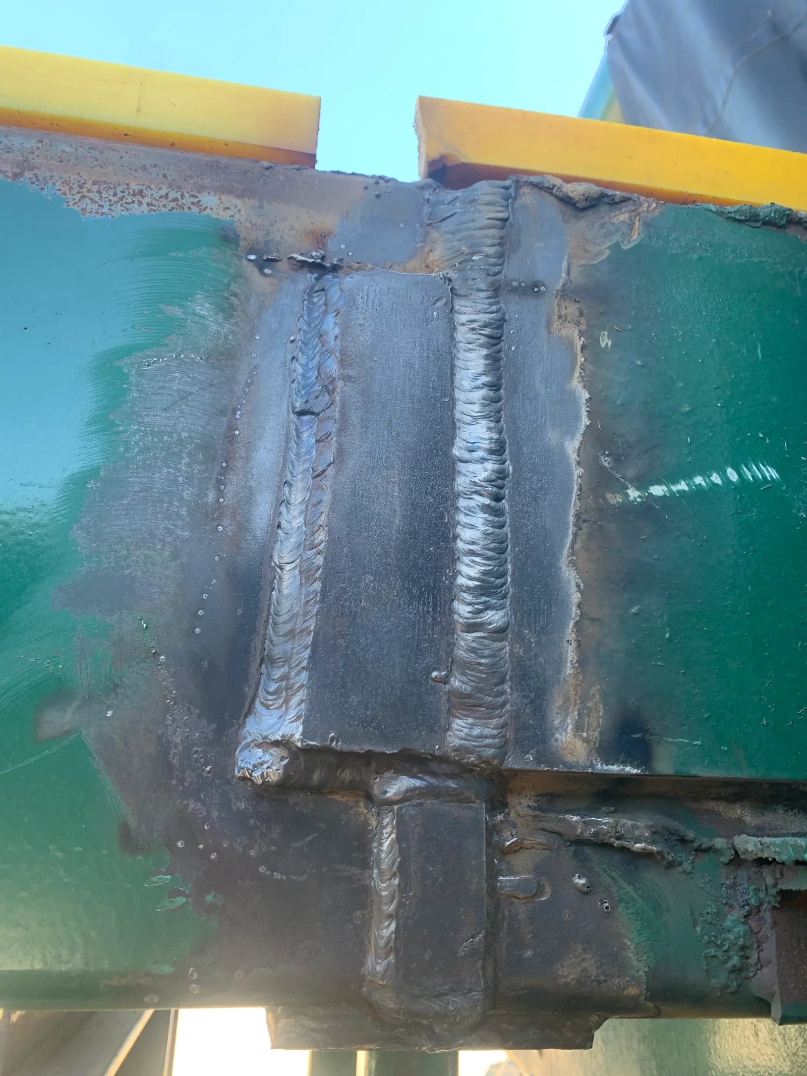Multi-pass arc welds on thick steel structural members with turquoise and yellow paint