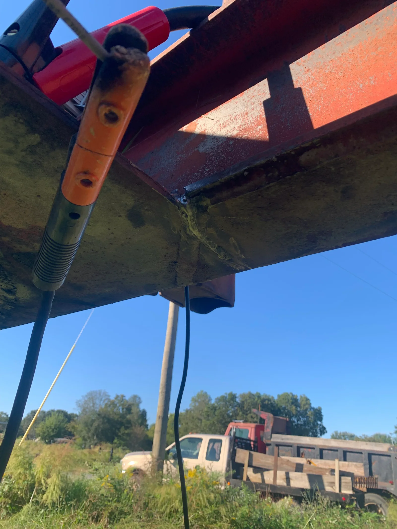 Hydraulic cylinder with orange and gray components mounted on corroded farm equipment frame