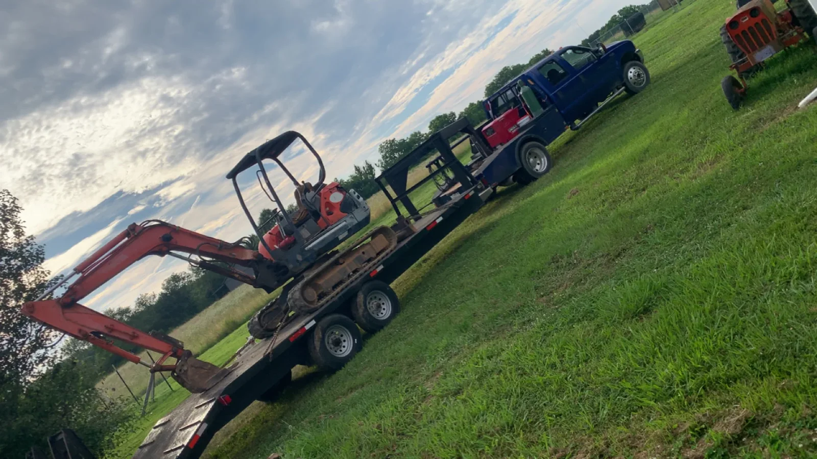 Red mini excavator on dual-axle flatbed trailer with hydraulic arm extended