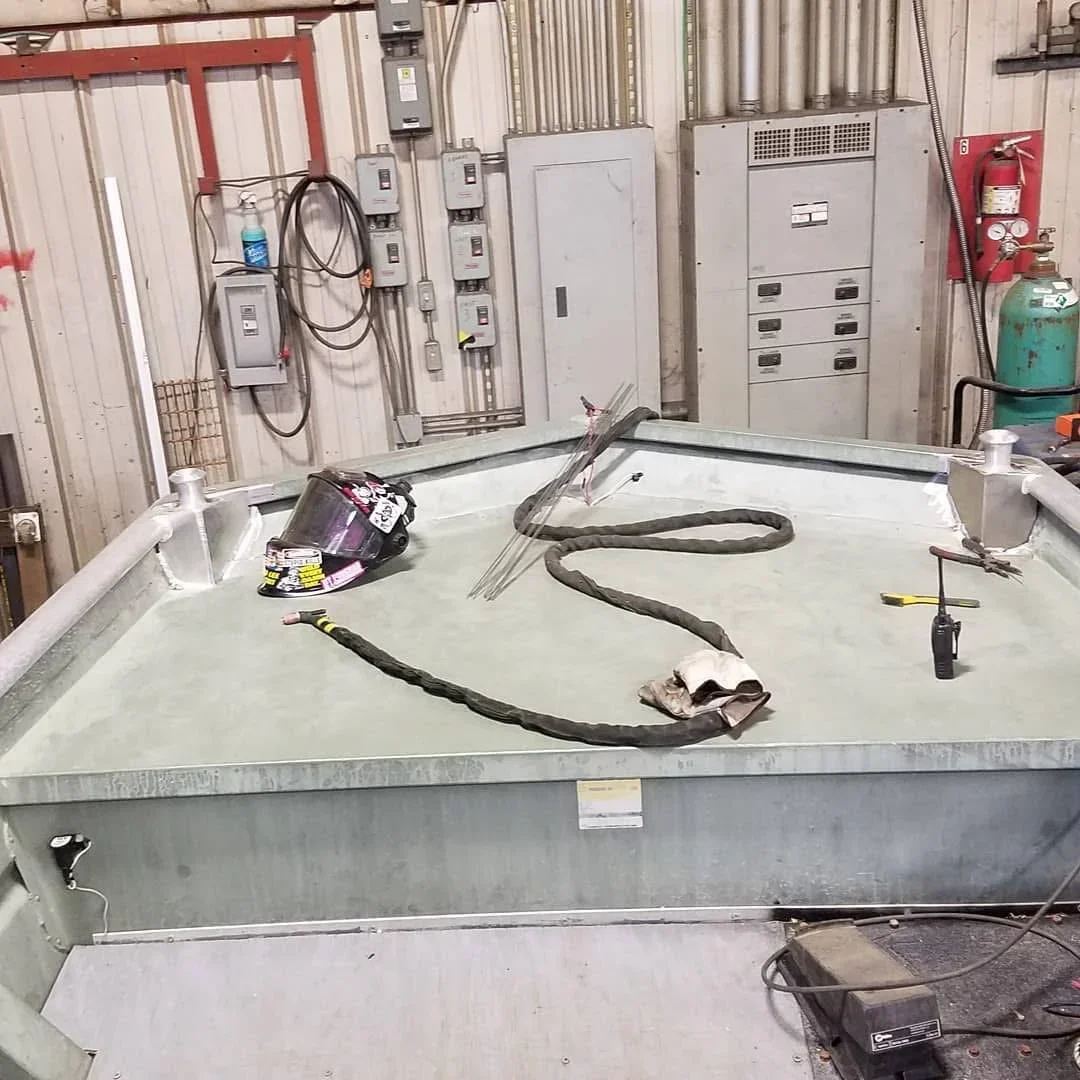 Industrial HVAC ductwork sections and welding equipment in repair bay with electrical panels