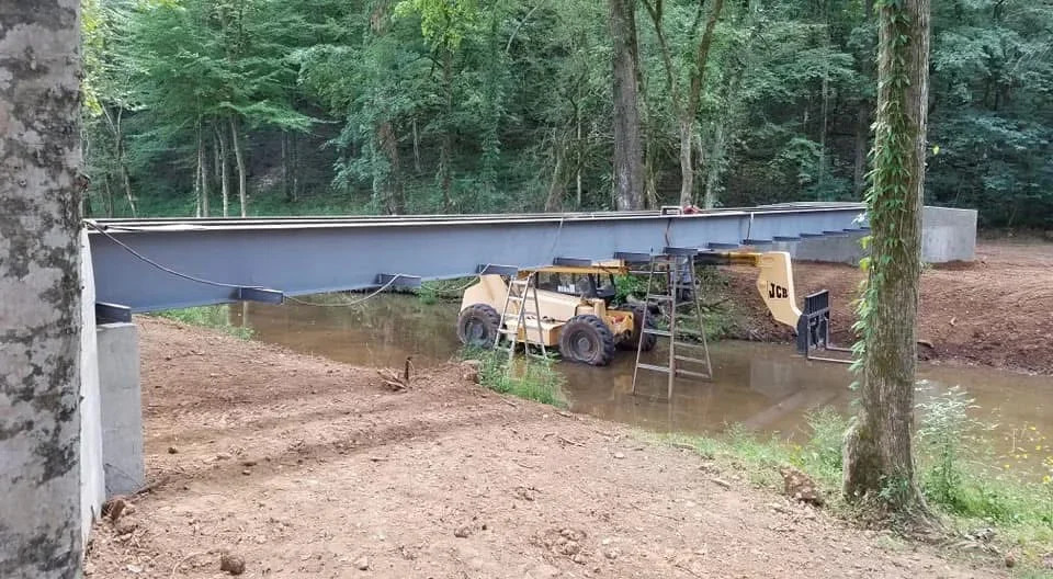 Blue HDPE pond liner with welded metal support framework and equipment staging in wooded area