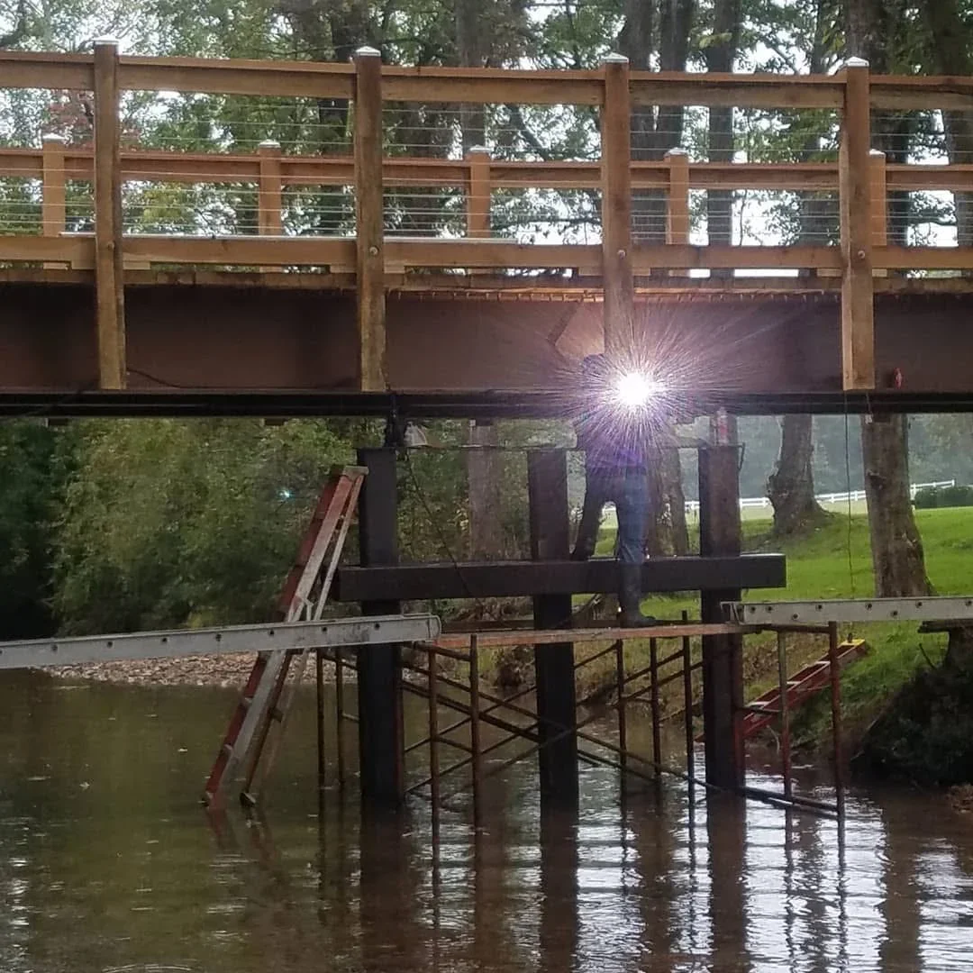 Steel I-beam welding on bridge structure over water with timber frame and support columns