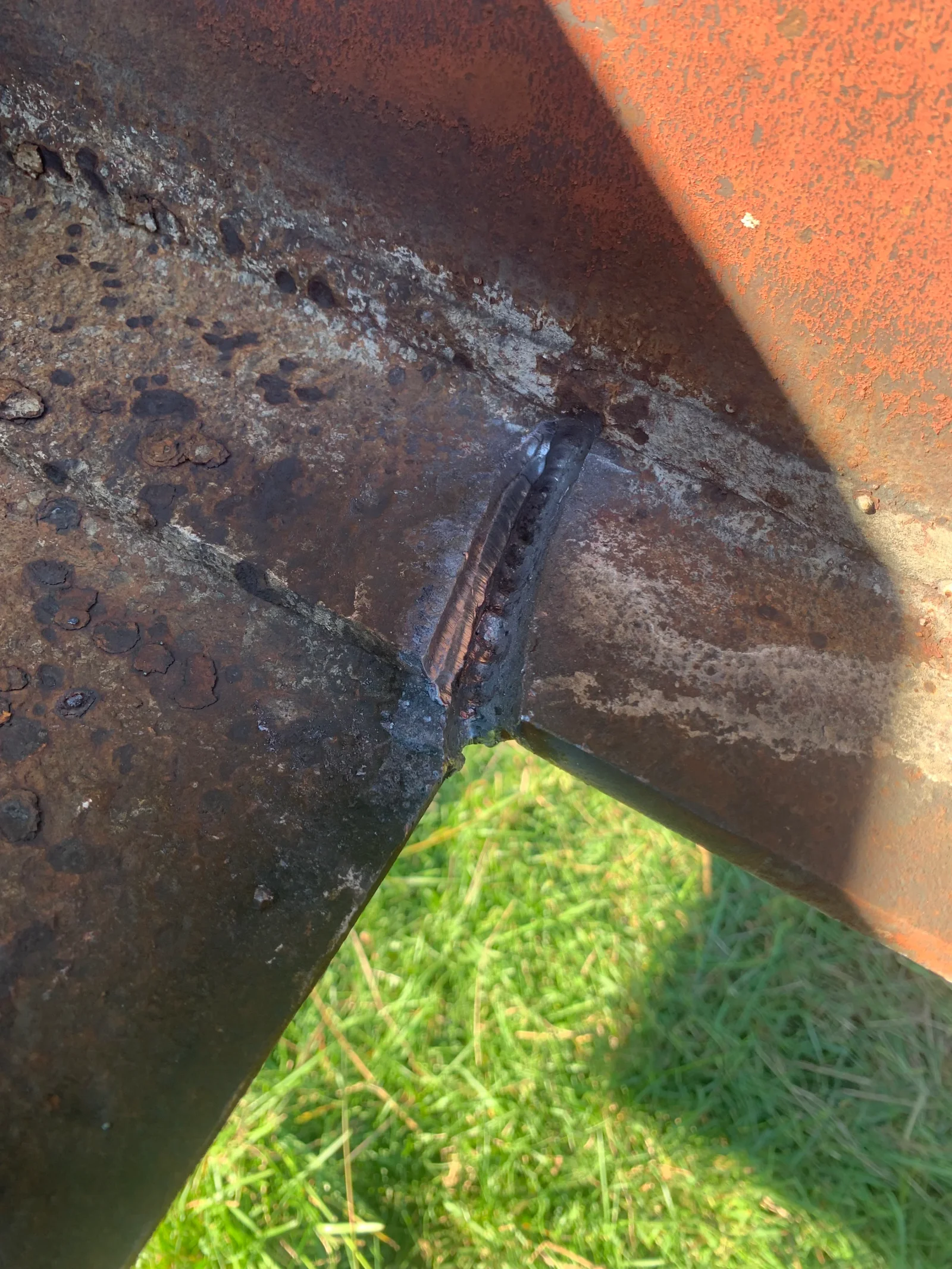 Corroded steel beam with rust pitting and welded repair joint, before restoration